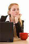 Attractive young blond woman in business suit leaning on hand sitting at a desk beside a big red coffee cup