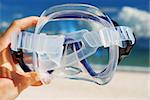 Snorkel equipment in hand against beach and sky