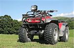Red and black four wheel drive quad bike standing on the grass in a field in summer with rural countryside and a blue sky to the rear