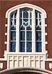 Church window has elaborate archetecture.  Below window crosses and shield dresses window casing.  Stained glass arched window.