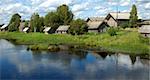 Northern russian village by the river, green grass, blue sky, reflections in water