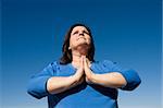 Woman praying outdoors against a vivid blue sky.