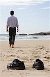 Manager walking barefoot on the beach. Focus on the shoes in the foreground
