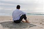 Businessman contemplating the sea while sitting barefoot on a rock on the beach
