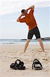Man doing gymnastics on the beach. Focus on his sandals in the foreground