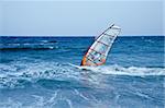 windsurfer sailing away form the beach on blue waters