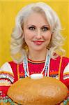 Close up a beautiful russian woman in a folk russian dress Holds a bread on yellow background