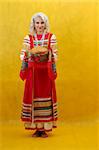 Russian woman in a folk russian dress Holds a bread on yellow background