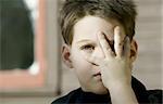 Close up of a young boy with his hand covering one eye.