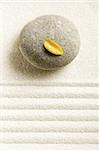 Stone on raked sand with a yellow leaf on a top. Zen concept