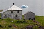 The natural beauty of the ocean, and an iceberg is contrasted with the economic reality of outmigration in Newfoundland. Pictured here is an abandoned house and shed, left to weather in the elements on the Bonavista peninsula.