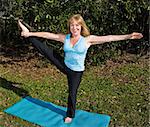 Beautiful sixty year old woman standing on one leg and stretching in a pilates pose.