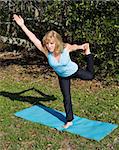 Beautiful 60 year old woman doing advanced pilates pose in a natural setting.