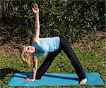 Beautiful, fit woman in her sixties doing the triangle yoga asana, outdoors in a natural setting.