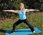 Fit beautiful sixty year old woman doing the warrior pose in yoga in a natural setting.