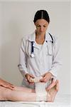 Young female doctor wrapping a female patient's ankle with a bandage. Isolated.