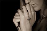 Young female prayer with rosary in sepia.