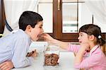 little girl in the kitchen giving a cookie to her brother