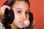Young girl listening to music and making a bubble from chewing gum