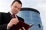 Young businessman smiling and taking notes in front of a corporate building