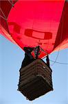 A man is standing in his hot air balloon waving with his hand.