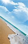 Sea waves on tropical beach and clouds with sun rays in the background