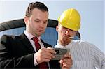 Young businessman showing something on a cell phone(PDA), to a construction worker in front of a corporate building