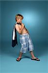 Boy in baggy blue plaid shorts with his shirt slung over one shoulder.