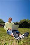 Young man, laying on grass with a laptop, surfing the net.
