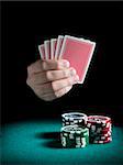 A man's hand holding four cards over three piles of different colors chips on a green felt.