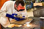 Worker using an acetylene torch to cut through metal in a metalworks factory.