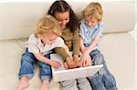 Three young children using a laptop together while sitting on a settee