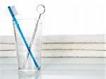 A blue toothbrush and a mouth mirror in a glass on a background with a few towels.