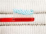 A red toothbrush full of toothpaste with white towels as background.