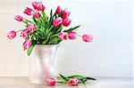 Pink tulips in white metal container against kitchen tiles