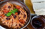 A plate of spaghetti with italian sauce, served with red wine, bread and olives on a wooden table
