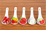 Assortment of candies in the spoons with soft shadow in the wooden background