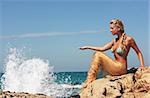Blond beauty girl sitting on the rocky beach