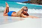 Happy blond girl lying on the beach in the waves
