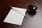 Ink, quill and an empty page on brown desk