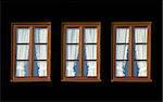 Three windows with white curtains in black background.
