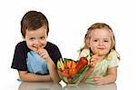Happy kids with a bowl of vegetables, smiling and eating carrot - isolated