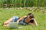 cute brunette in casual dress laying down on the grass and working on the computer