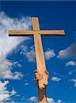 A man´s hand keeping a wooden cross high in the sky.