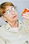 Elderly woman reading pill bottle label with glasses