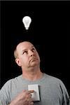 A man looking at a lighted lightbulb over his head.