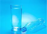 A glass of water and empty bottle on blue background