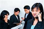 Young Chinese businesswoman talking on the phone while the other business people busy on the background.