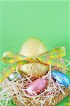 Assortment of chocolate Easter eggs wrapped in colorful paper in the basket with straw