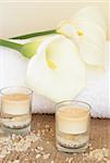 Relaxing spa scene with a white rolled up towel, white lillies, beautiful handmade candles and bath salts